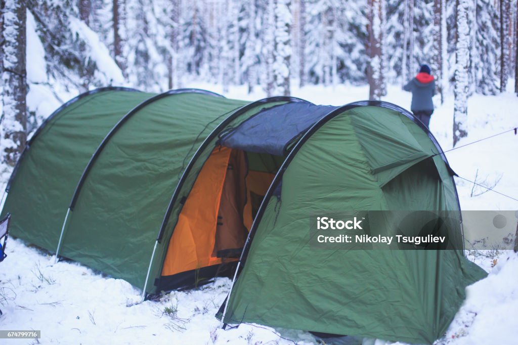 A process of camping in winter forest, setting a tent covered in snow, making a bonfire campfire and cooking food with portable gas cooker and fire, snowy landscape A process of camping in winter forest, setting a tent covered in snow, making a bonfire campfire and cooking food with portable gas cooker and fire, snowy landscape, scandinavia Adventure Stock Photo