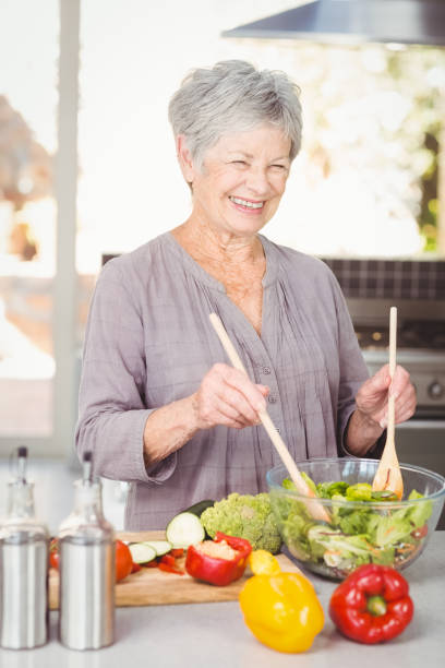 istock Happy senior woman tossing salad while standing in kitchen 674818654