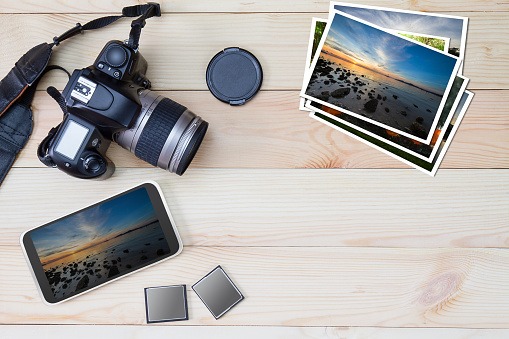 DSLR camera, smartphone, photos and memory card on wooden background