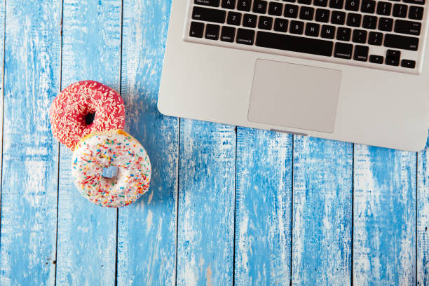 istock Top view of laptop with donuts on wooden table 674895940