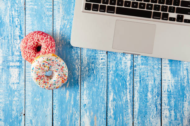 istock Top view of laptop with donuts on wooden table 674896486