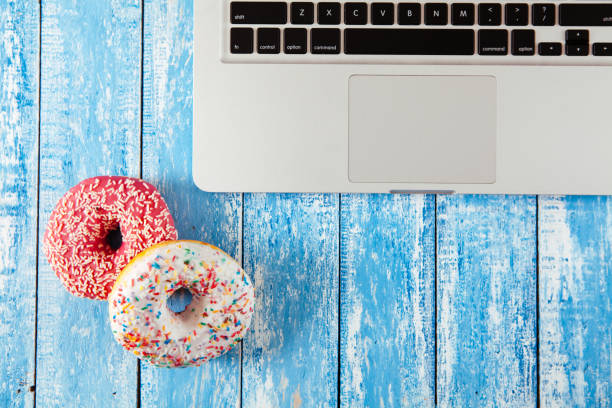 istock Top view of laptop with donuts on wooden table 674899082
