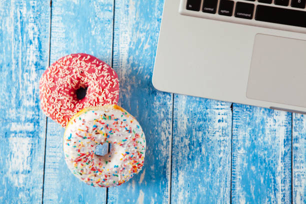 istock Top view of laptop with donuts on wooden table 674899258