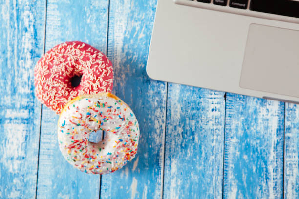 istock Top view of laptop with donuts on wooden table 674899722