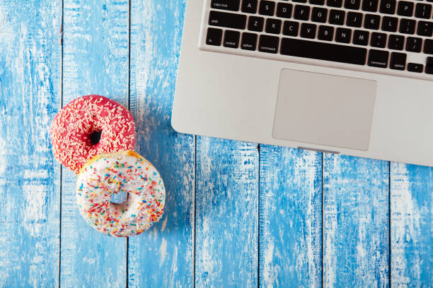 istock Top view of laptop with donuts on wooden table 674899738