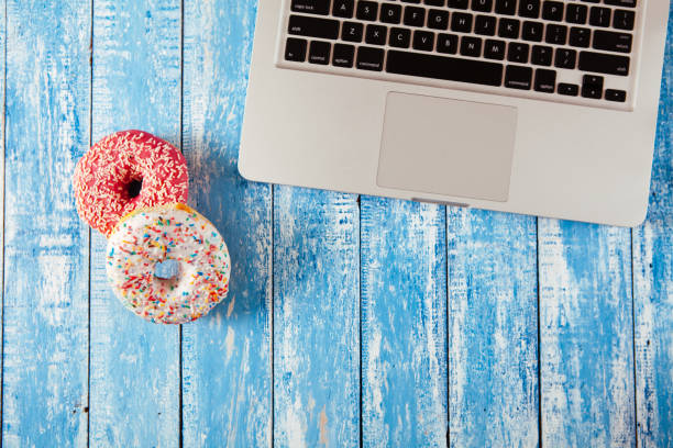 istock Top view of laptop with donuts on wooden table 674899756