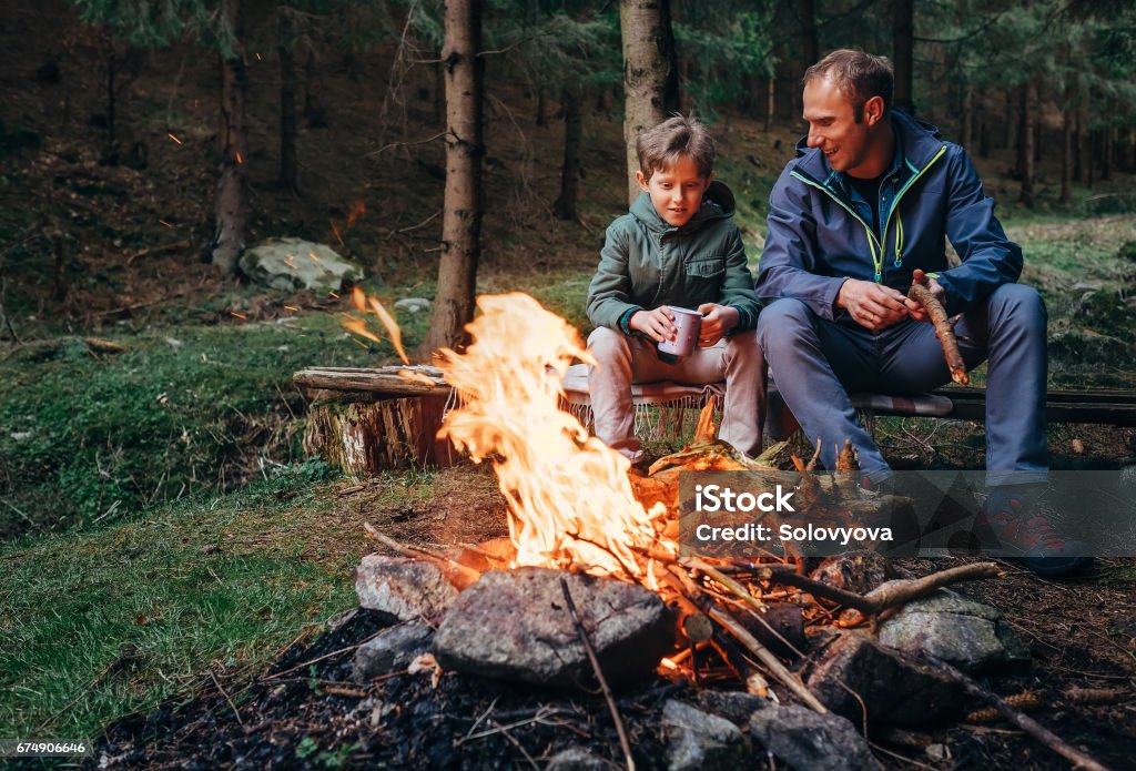 Vader met zoon warm in de buurt van kampvuur, drinken thee en gesprek - Royalty-free Kamperen Stockfoto