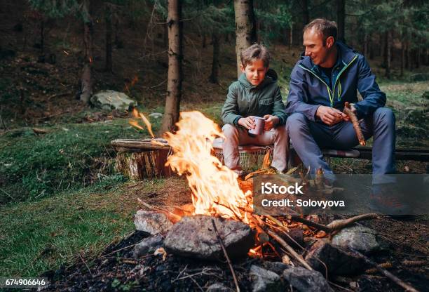 Vader Met Zoon Warm In De Buurt Van Kampvuur Drinken Thee En Gesprek Stockfoto en meer beelden van Kamperen