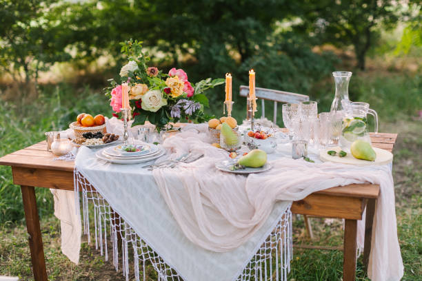 istock picnic, summer, holiday concept - beautiful decorated table at green lawn with trees, openwork white tablecloth, colorful bouquet of peony flowers and roses, glassware, fruits, candlesticks, lemonade 674916834