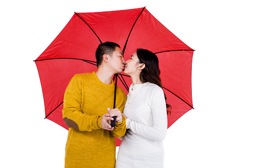 Couple kissing under umbrella against white background