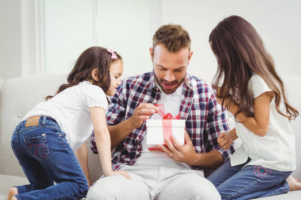 istock Curious girls looking at father opening gift 674924320