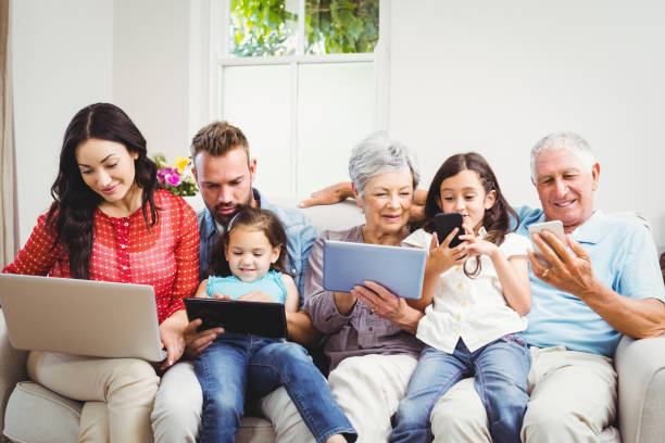 famiglia che utilizza le tecnologie mentre è seduta sul divano - grandparent family multi generation family technology foto e immagini stock