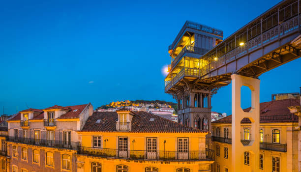 Lisbon Elevador de Santa Justa Castelo de Sao Jorge Portugal The iconic ironwork of the Elevador de Santa Justa illuminated at dusk overlooking the lamplit streets of Baixa and the iconic battlements of the Castelo de Sao Jorge in the heart of Lisbon, Portugal’s vibrant capital city. santa justa lift portugal stock pictures, royalty-free photos & images