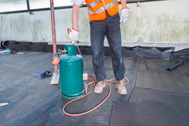 Worker, with a roofing gas torch, is installing rolls of bituminous waterproofing membrane for the waterproofing of a terrace - roof of a home