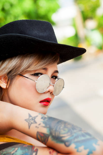 Facial portrait of thai girl with hat and tattoos Facial portrait of thai girl with hat and tattoos standing in street in Bangkok sonnenbrille stock pictures, royalty-free photos & images