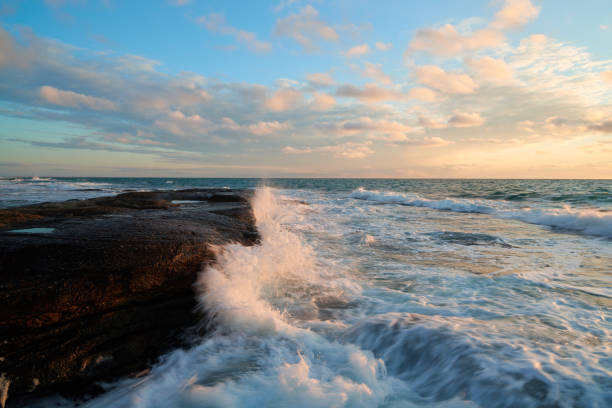 Autumn sunrise with the sun's rays beaming through the clouds over the sea and rocks at The Skillion in Terrigal, NSW, Australia.