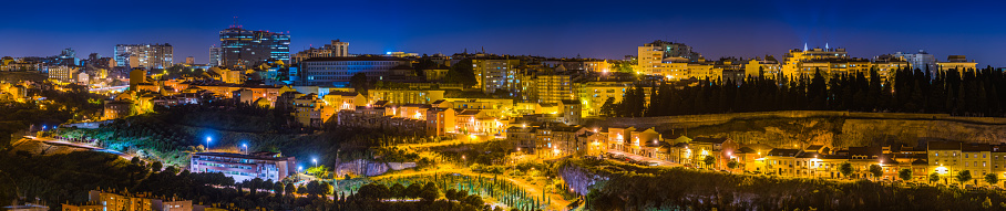 Panoramic view across parkland and dusty roads, apartment buildings and highrise offices along the illuminated city skyline of Lisbon, Portugal at night.