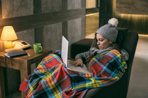 mujeres vestidas de invierno cap trabajo en portátil envuelto en una cobija en su casa sin calefacción - women computer home interior brown hair fotografías e imágenes de stock