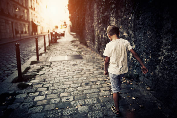 Depressed little boy walking narrow cobblestoned street of Paris Montmartre.\n