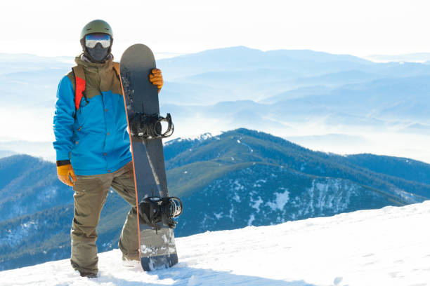 istock Young snowboarder standing next to snowboard thrusted into snow with beautiful scenery on background 674967172