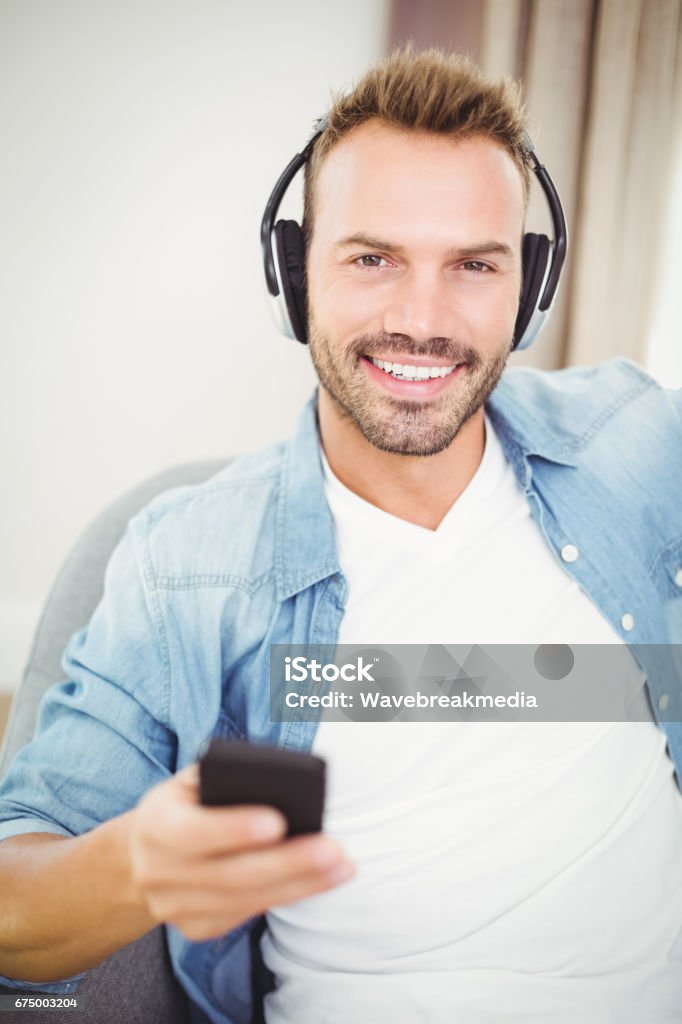 Portrait of smiling man listening to music while holding mobile phone Portrait of smiling man listening to music while holding mobile phone at home 30-39 Years Stock Photo