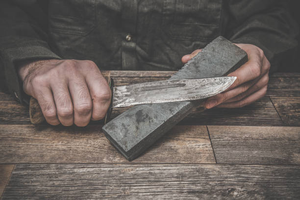 istock Man's hands sharpening old knife on the wooden table. Dark, vintage atmosphere. 675024242