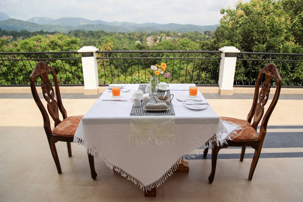 Dining table covered with white cloth, prepared for breakfast, outdoor on balcony with a view on the green nature in Sri Lanka