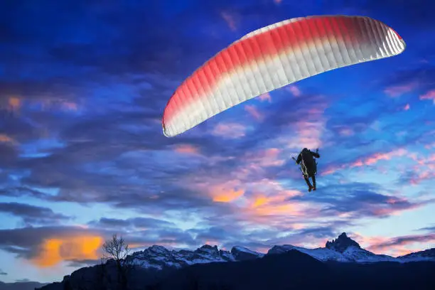 Photo of Paraglider flying over mountains in winter sunset