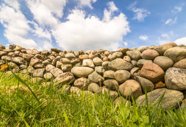istock Old Stone wall with green grass in front and blue sky with clouds above 675055450