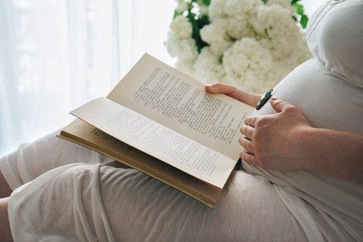 Pregnant woman touching her belly while she is readind a book