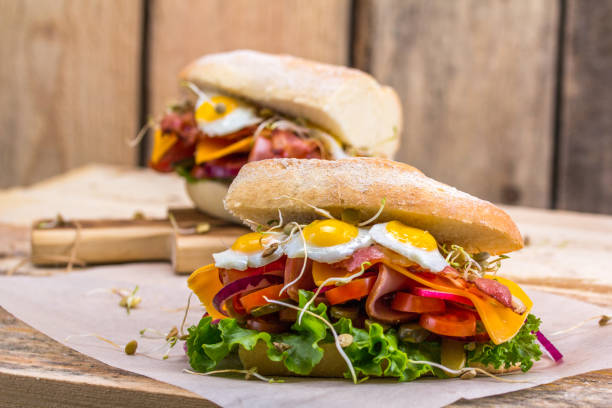 istock A sandwich with bacon, cheese and fried quail eggs. A sandwich with fresh vegetables and herbs on a wooden background. 675061554