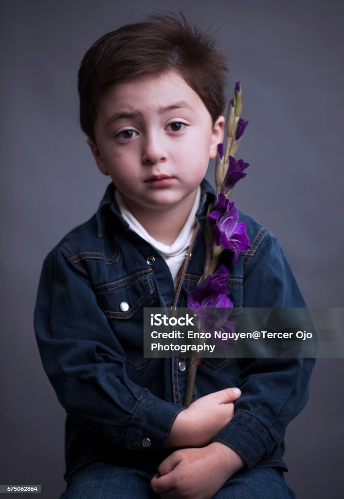 Portrait of a unhappy and serious looking mixed race asian caucasian little boy wearing a blue denim jacket and white shirt holding a purple iris flower Adult Stock Photo