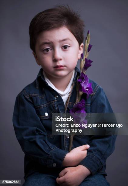 Portrait Of A Unhappy And Serious Looking Mixed Race Asian Caucasian Little Boy Wearing A Blue Denim Jacket And White Shirt Holding A Purple Iris Flower Stock Photo - Download Image Now