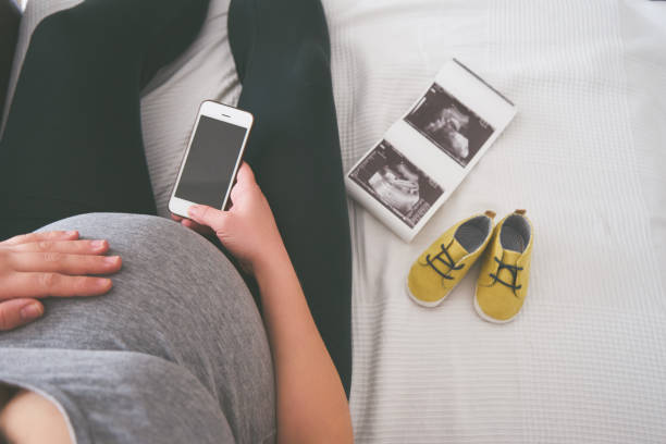 Jeune femme enceinte se relaxant sur un canapé avec téléphone intelligent - Photo