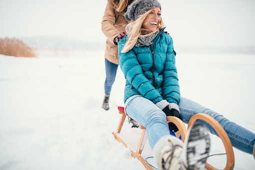Two girlfriends sledding in a winter day