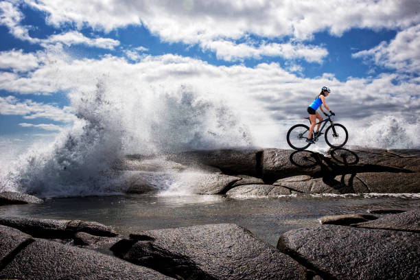Woman on mountain bike with ocean waves splashing in the background in Nova Scotia.
