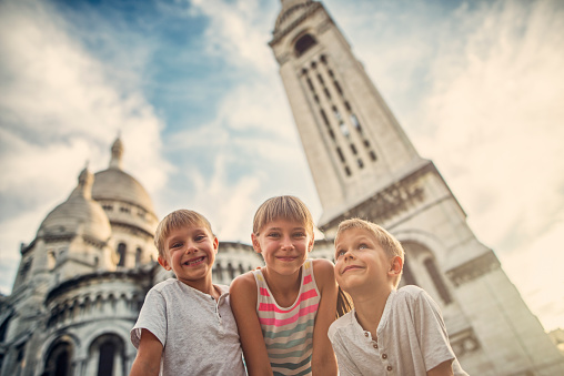 Three kids visiting Paris. They are holding hands and having fun in the beautiful parisian street. They are running towards the Basilica of Sacre Coeur. The girl is aged 9 and her brothers are aged 6.\n