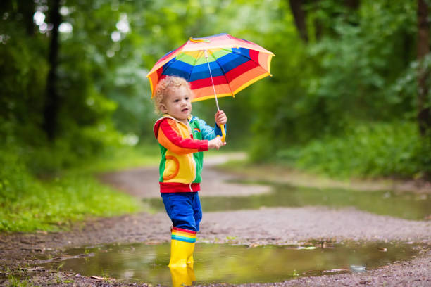 criança brincando na chuva sob guarda-chuva - 11892 - fotografias e filmes do acervo