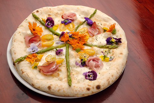 This pizza is decorated with edible flowers (flowers you can eat), as well as asparagus, cured ham and yellow cherry tomatoes (