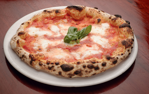 Amazingly good pizza margherita, in a simple white plate on a wooden table