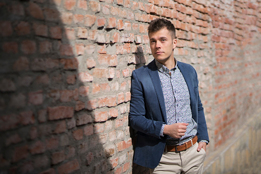 Fashion portrait of a handsome young man leaning on the brick wall.