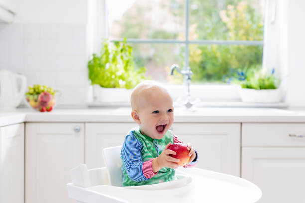istock Baby boy eating apple in white kitchen at home 675079138