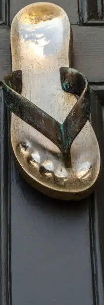 Photo of Brass knocker shaped flip-flops, beautiful ornament on brown wood