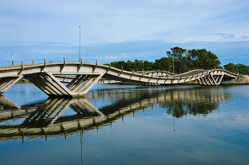 The image of a wavy bridge reflected above the river water