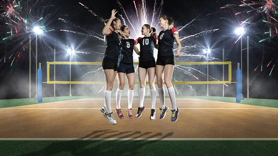 Female volleyball team celebrating victory on night volleyball field with fireworks on background
