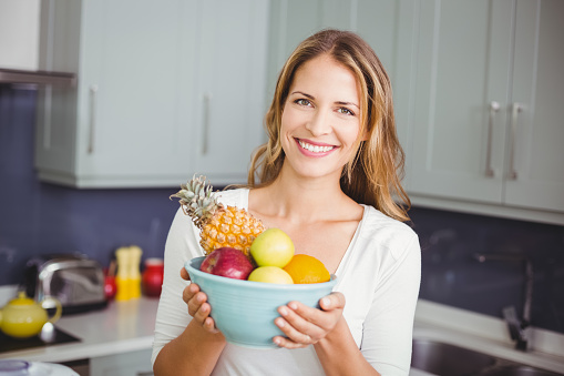 Portrait of smiling woman holding fruit bowl in kitchen