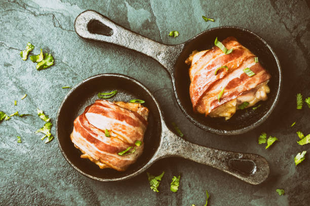 istock Baked chicken wrapped in bacon on cast iron pans. Top view 675085428