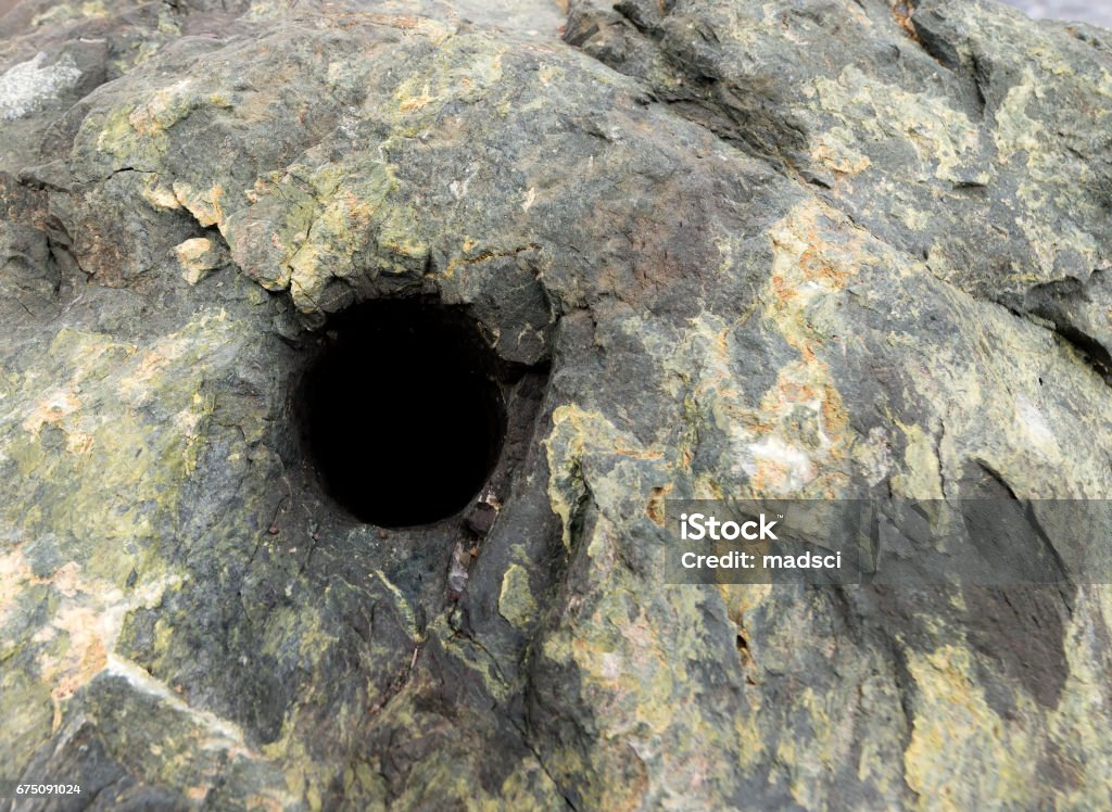 Blasting Hole In Rock Dark hole drilled in rock. This is the type of hole dynamite is put in to blast rocks and cliffs. The rock is mostly dark green. Focus is on the top edge of the hole. Room for text on the right. Quarry Stock Photo