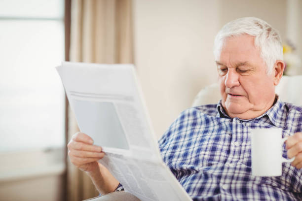 istock Senior man reading newspaper in living room 675091348