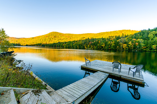 A small deck in the middle of a lake in Vermont.  Three chairs are on the deck, inviting people to have a rest